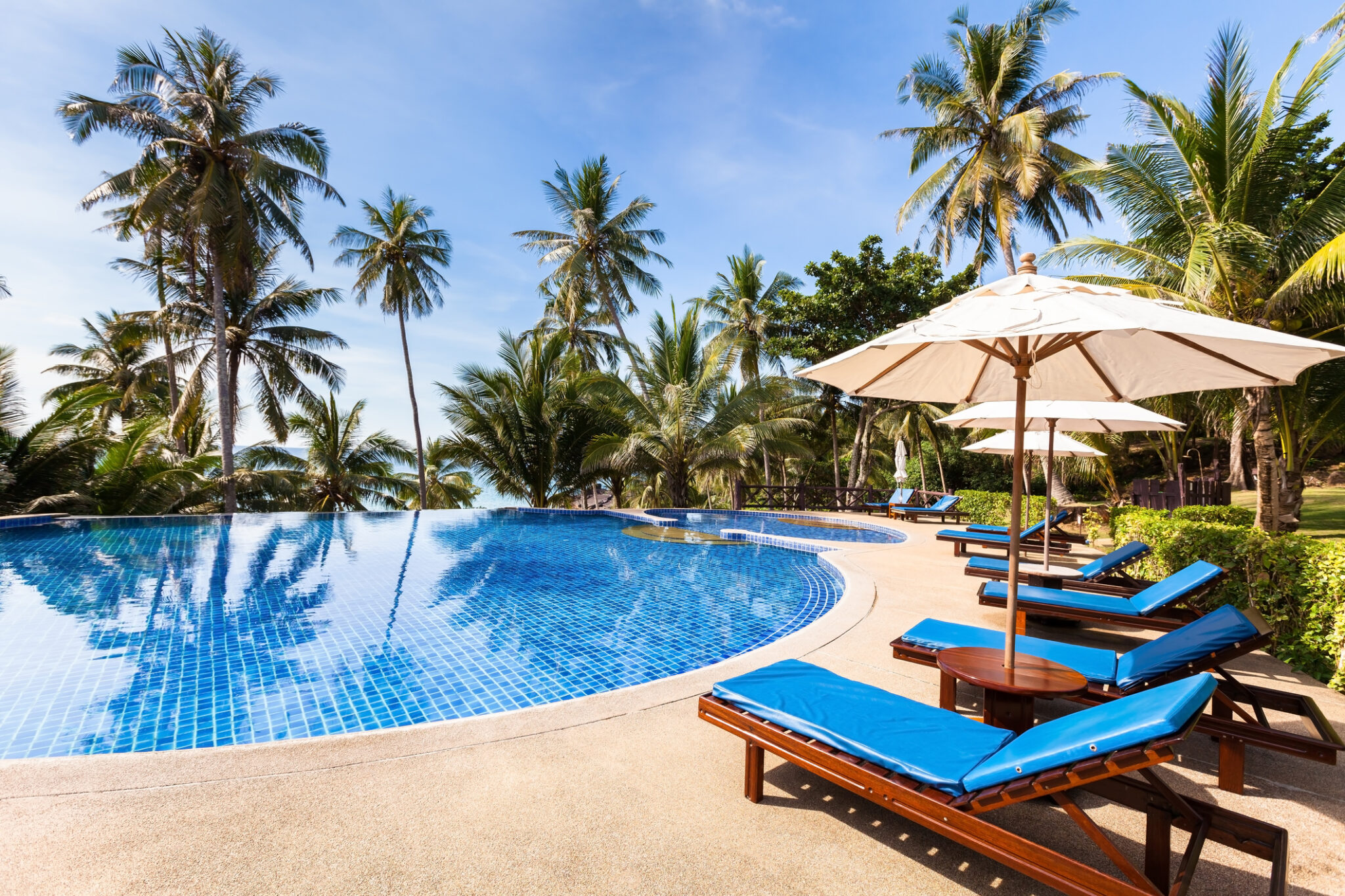 Beautiful tropical beach front hotel resort with swimming pool, sun-loungers and palm trees during a warm sunny day, paradise destination for vacations